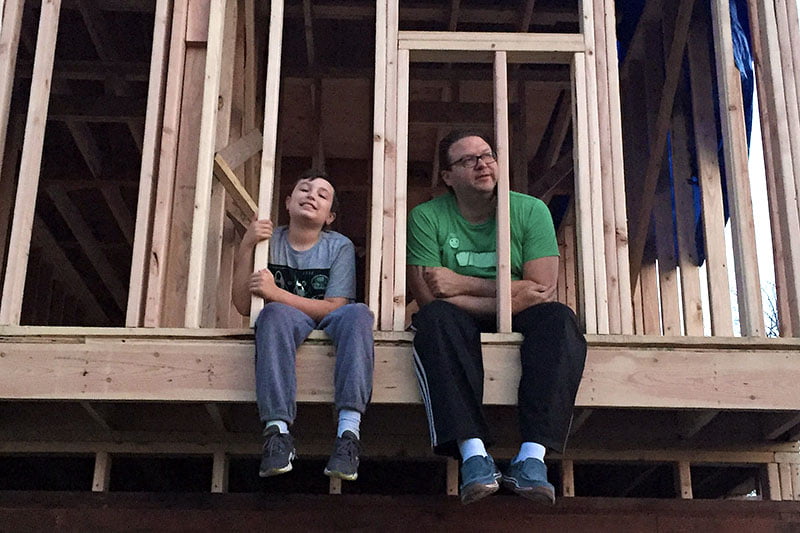 man and child sitting on edge of under-construction house