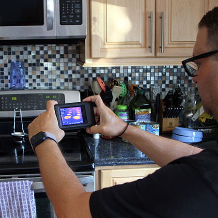 inspector in kitchen pointing thermal camera at stove