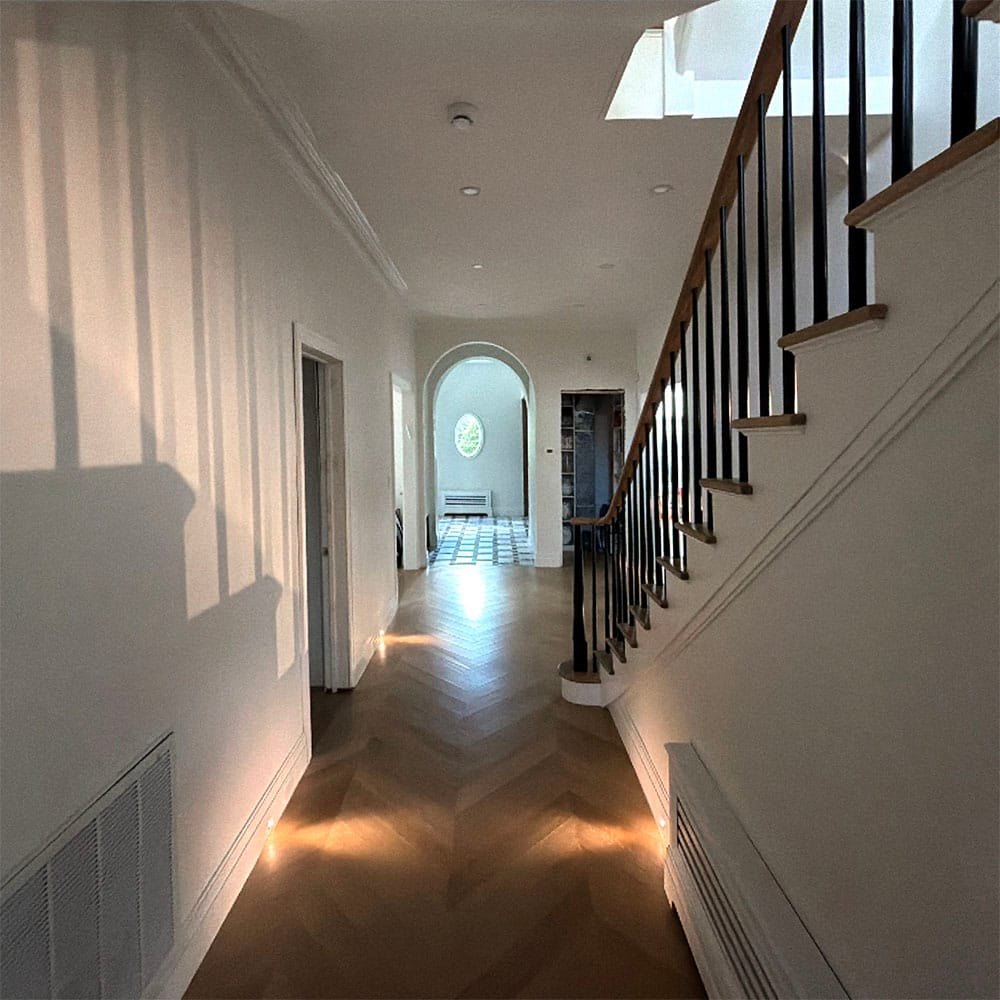 Interior shot documenting a staircase alongside a long hallway finished with hardwood floors.
