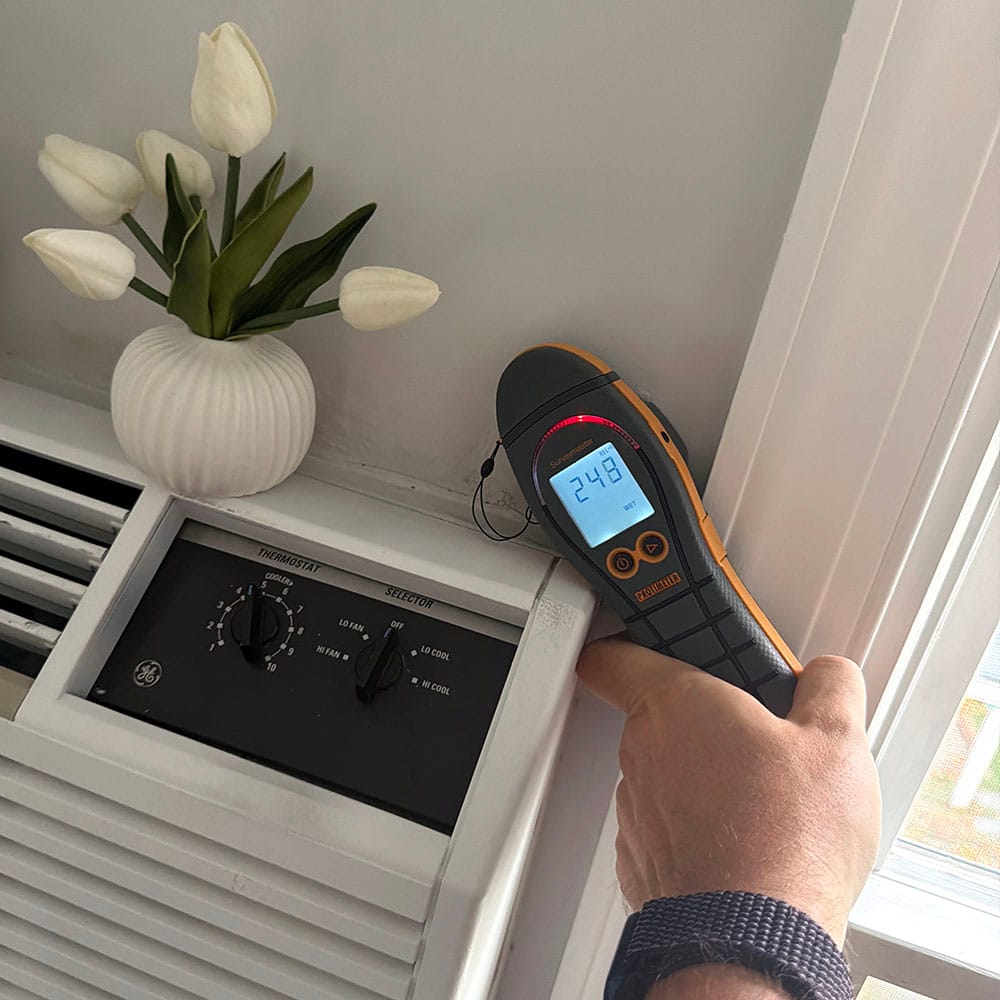 Close-up of a wall above an air conditioning unit showing water staining and a moisture meter reading "wet".